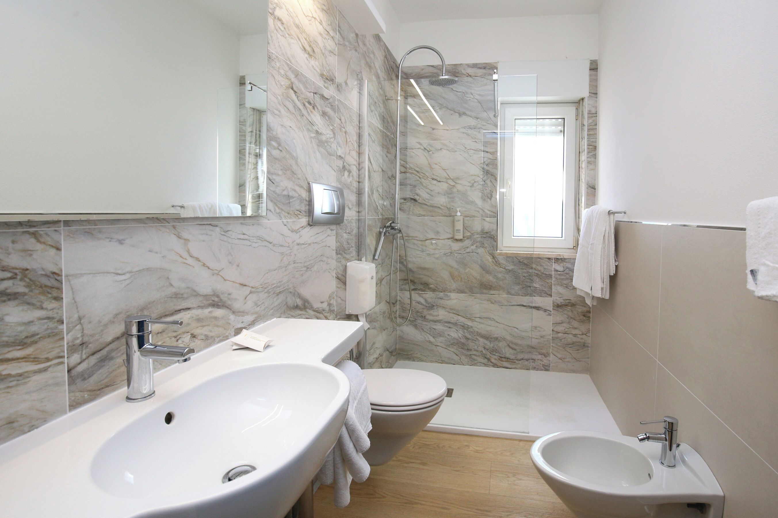Een moderne badkamer met een groot wastafel, toilet, bidet en douchegedeelte.