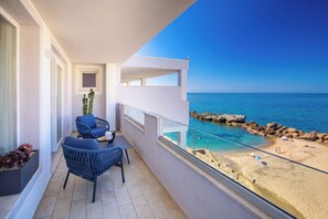 A balcony with a view of the sea, a chair, a small table, and a potted plant.