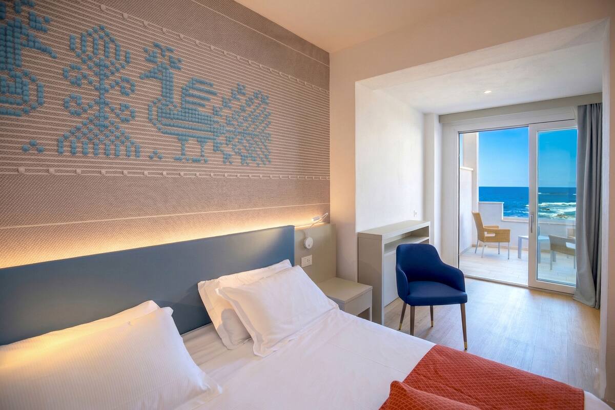 A hotel room with a bed, a desk, a chair, and a view of the ocean.