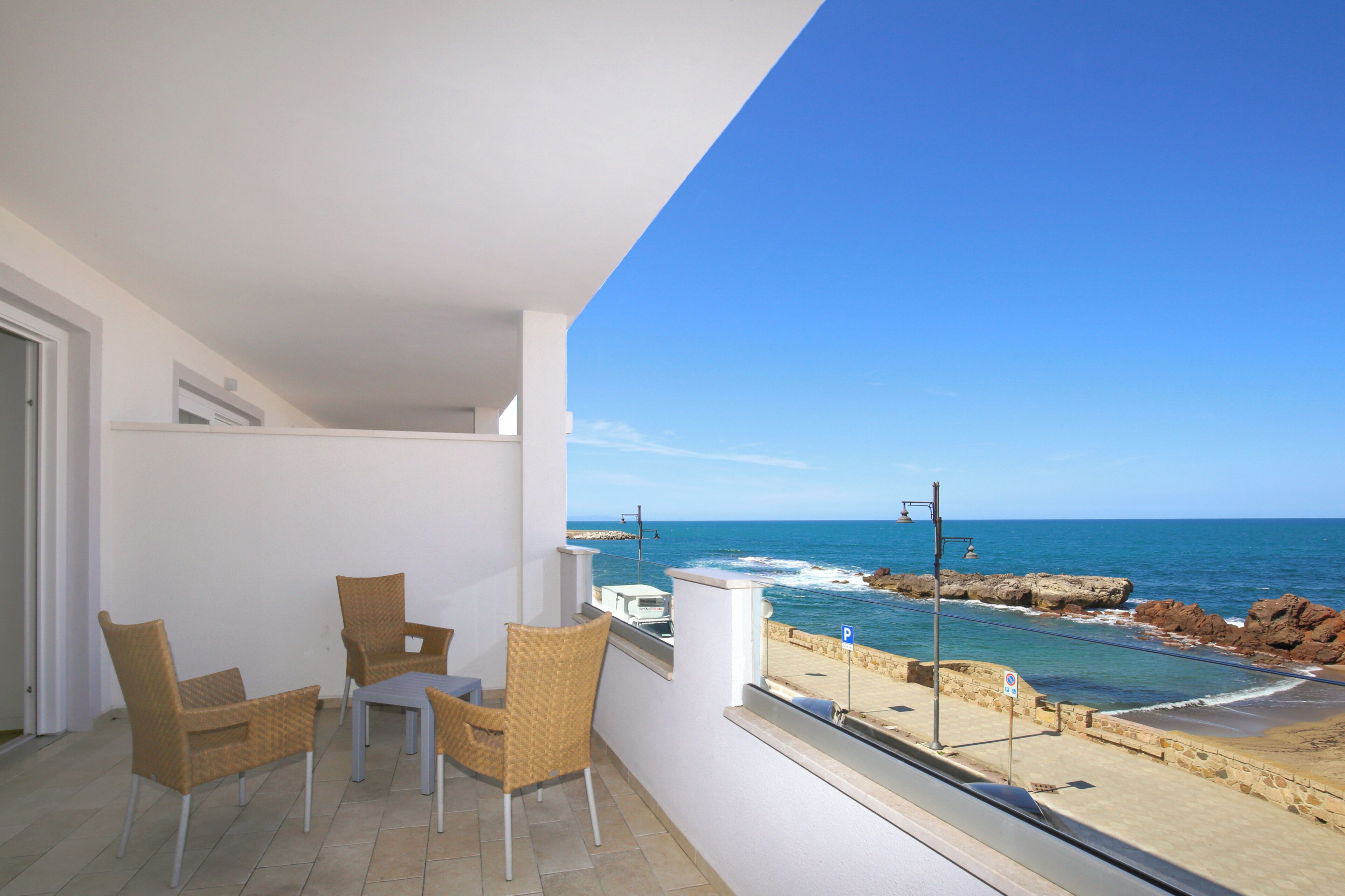 Un balcon avec des fauteuils en osier et une table, d’où l’on peut admirer un littoral rocheux et la mer.