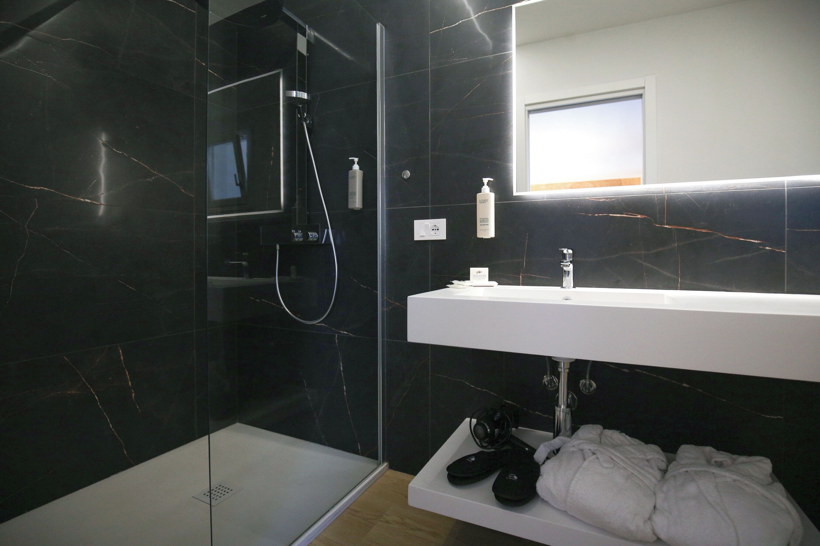 Un baño moderno con ducha envuelta en vidrio, un lavabo blanco y un espejo encima.