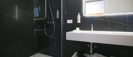 Un baño moderno con ducha envuelta en vidrio, un lavabo blanco y un espejo encima.