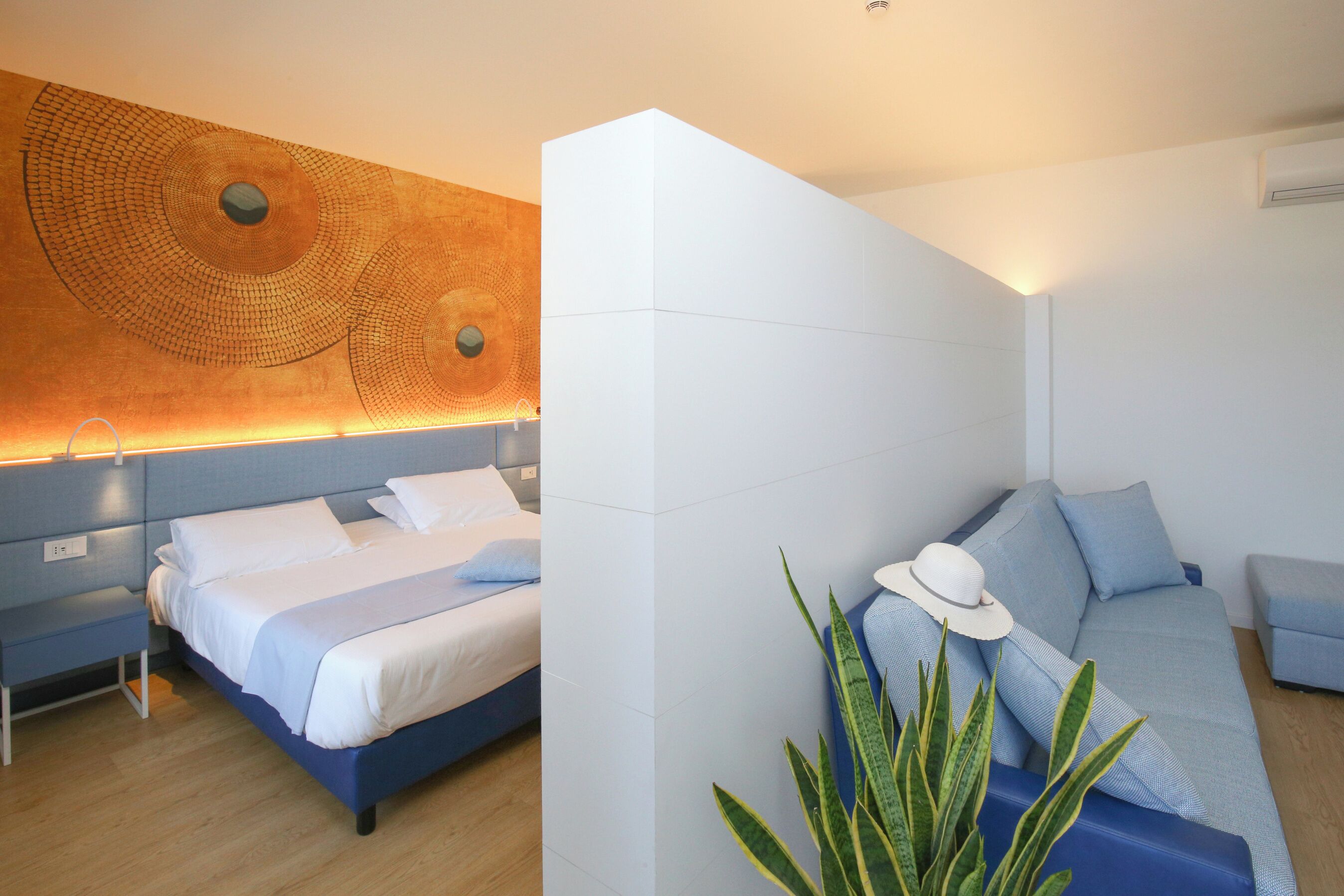 Una habitación de hotel moderna con una cama, un sofá, una obra de arte en la pared y una planta en maceta.