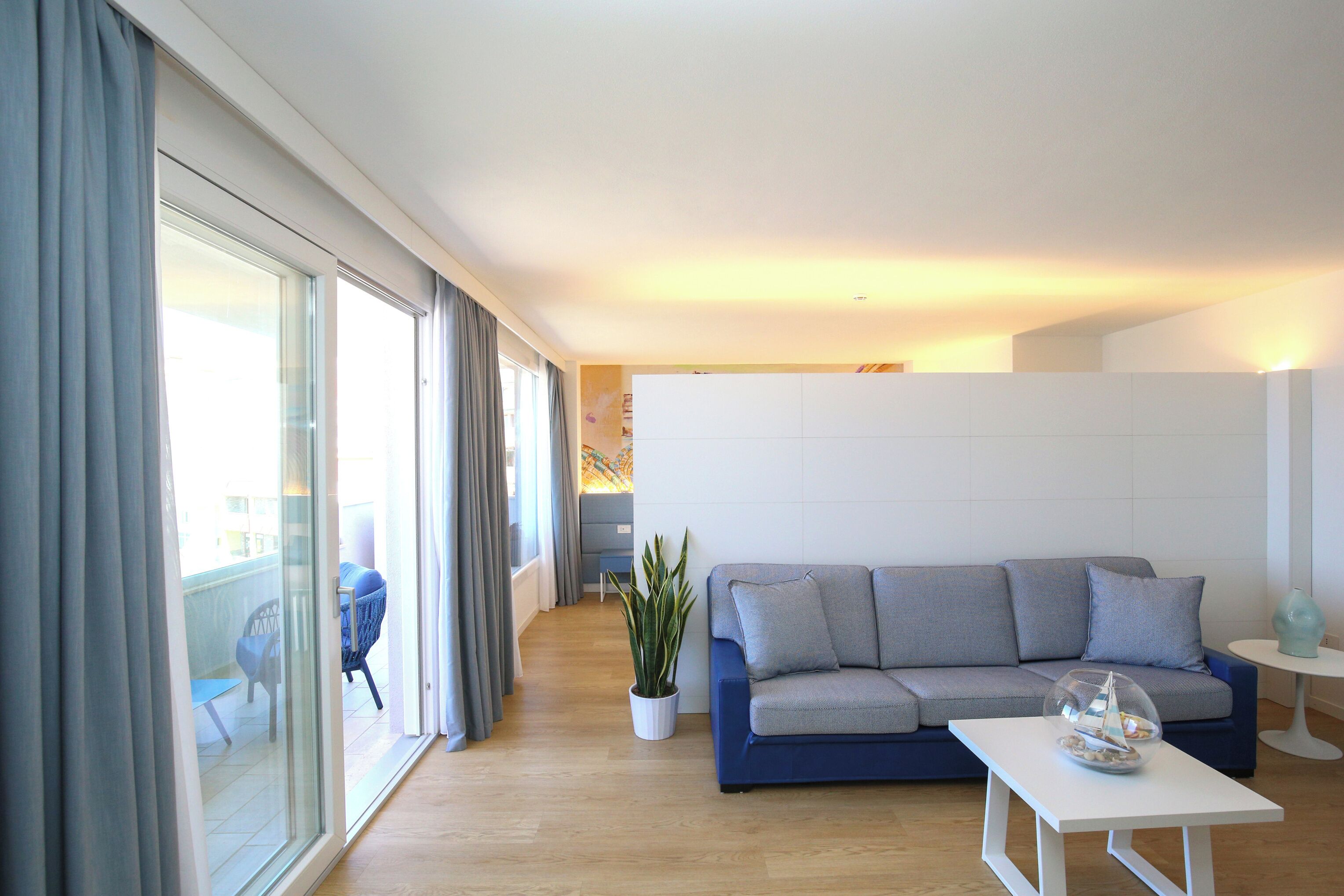 A modern living room with a sofa, a coffee table, a potted plant, and a sliding glass door leading to an outdoor area.