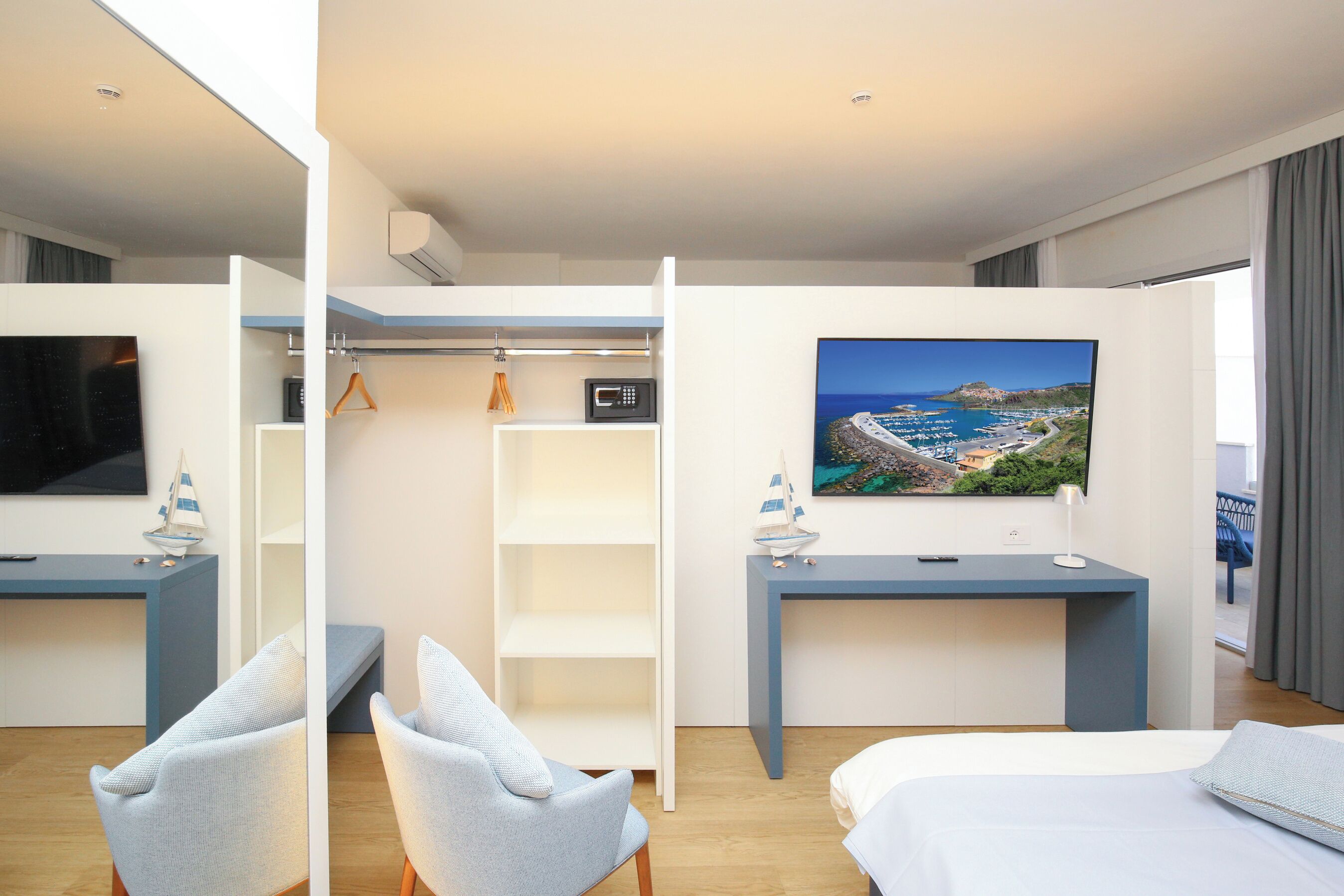 A modern hotel room with a bed, two seating areas, a desk, a TV, and a large window with a view.