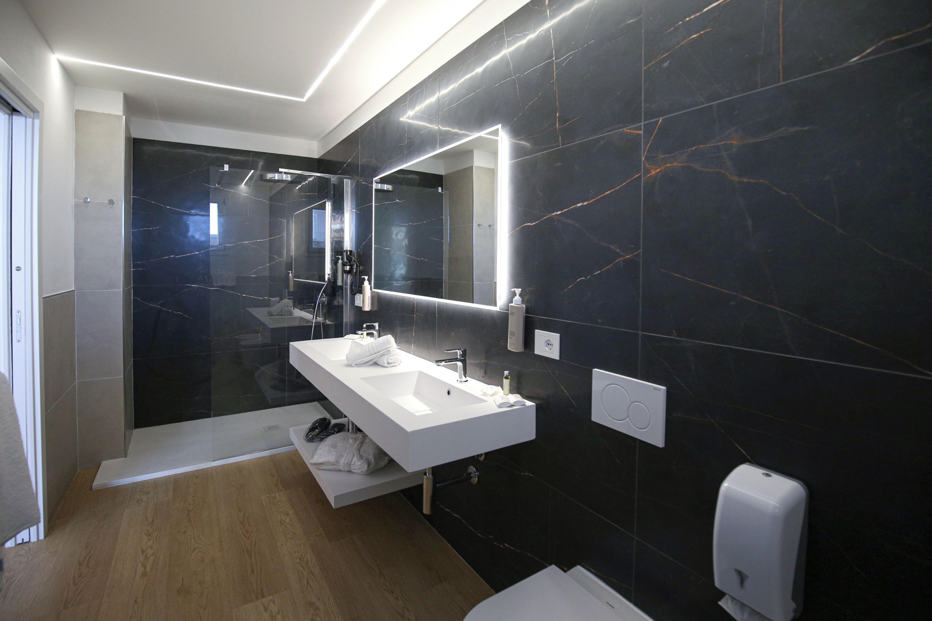 A modern bathroom with a white sink, a large mirror, and a marble wall.