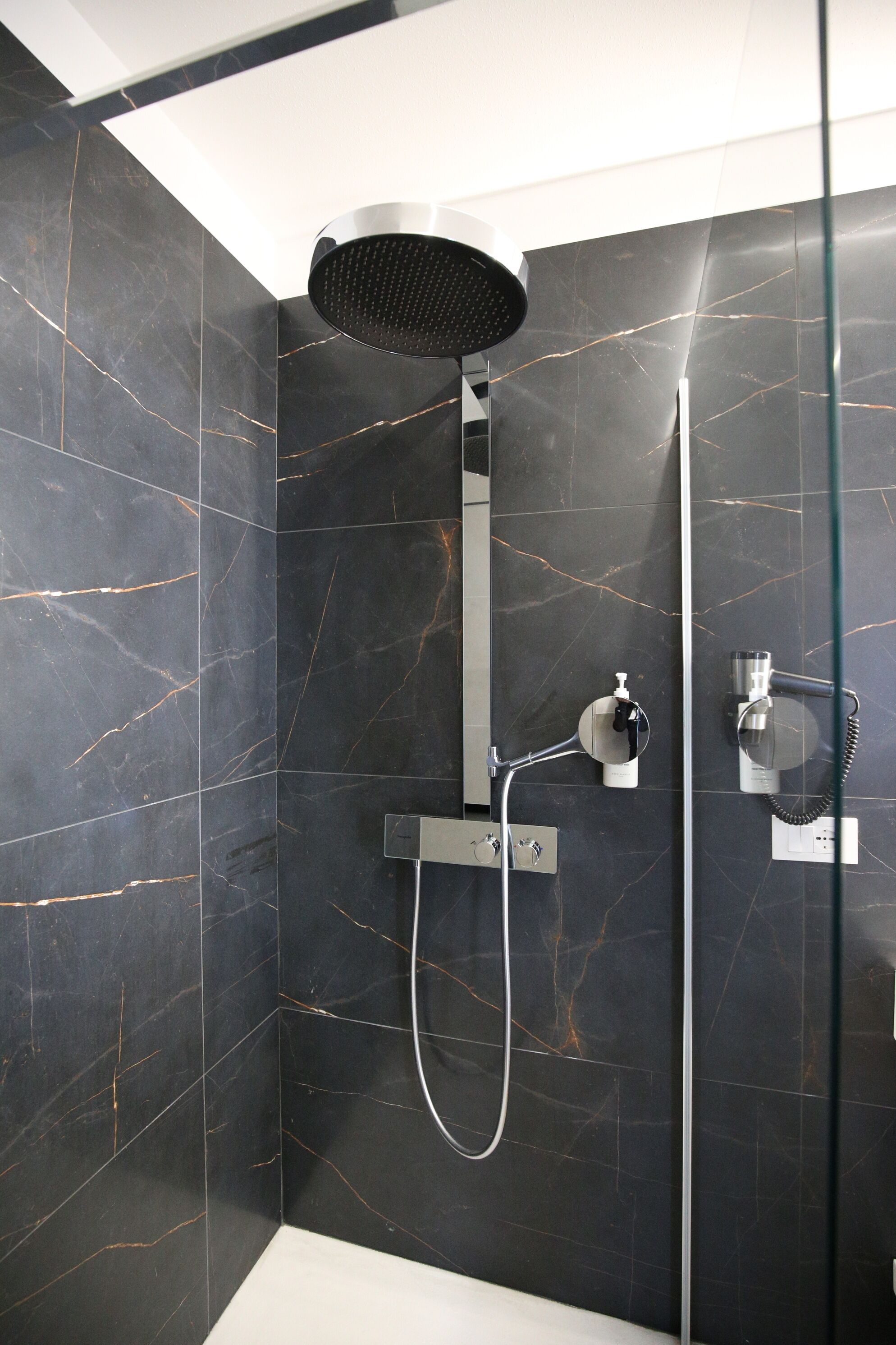 A modern shower with a handheld showerhead, a wall-mounted faucet, and a glass partition.