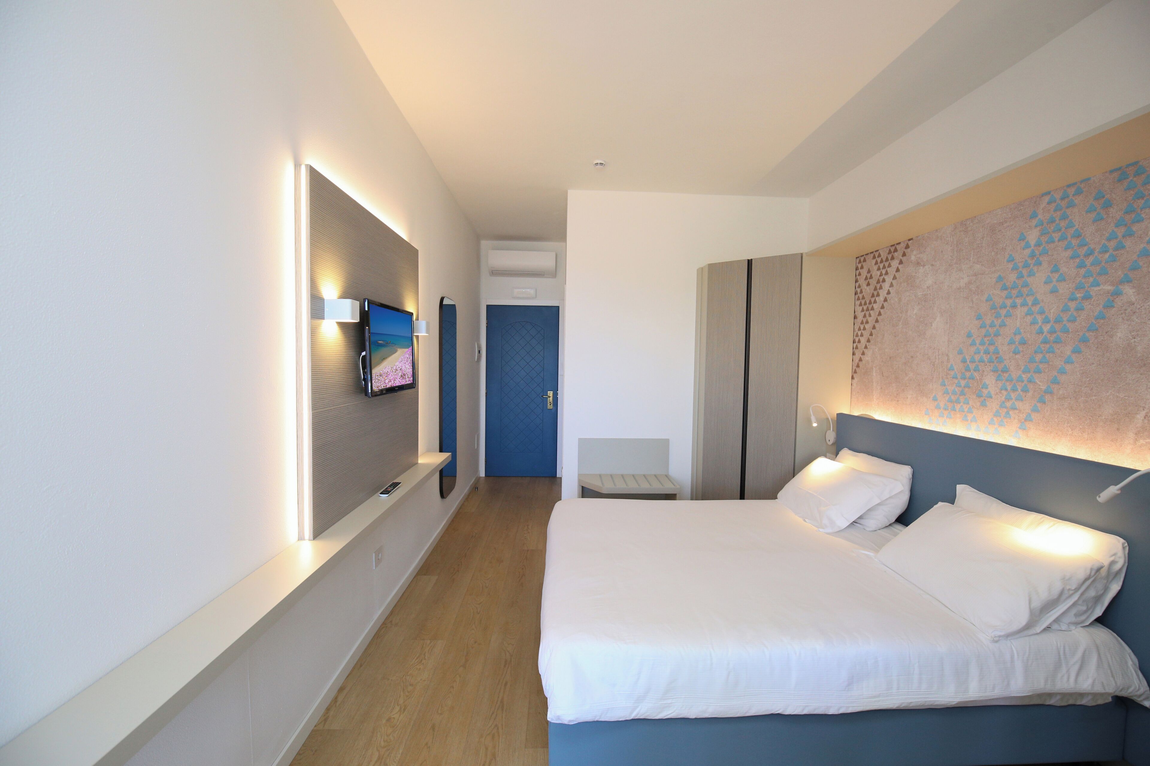 A modern hotel room with a bed, bedside table, and a wall-mounted TV.