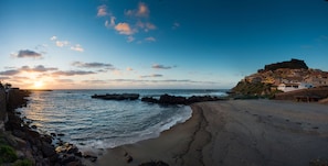 A coastal town with a beach, rocky shoreline, and a prominent hill with buildings.