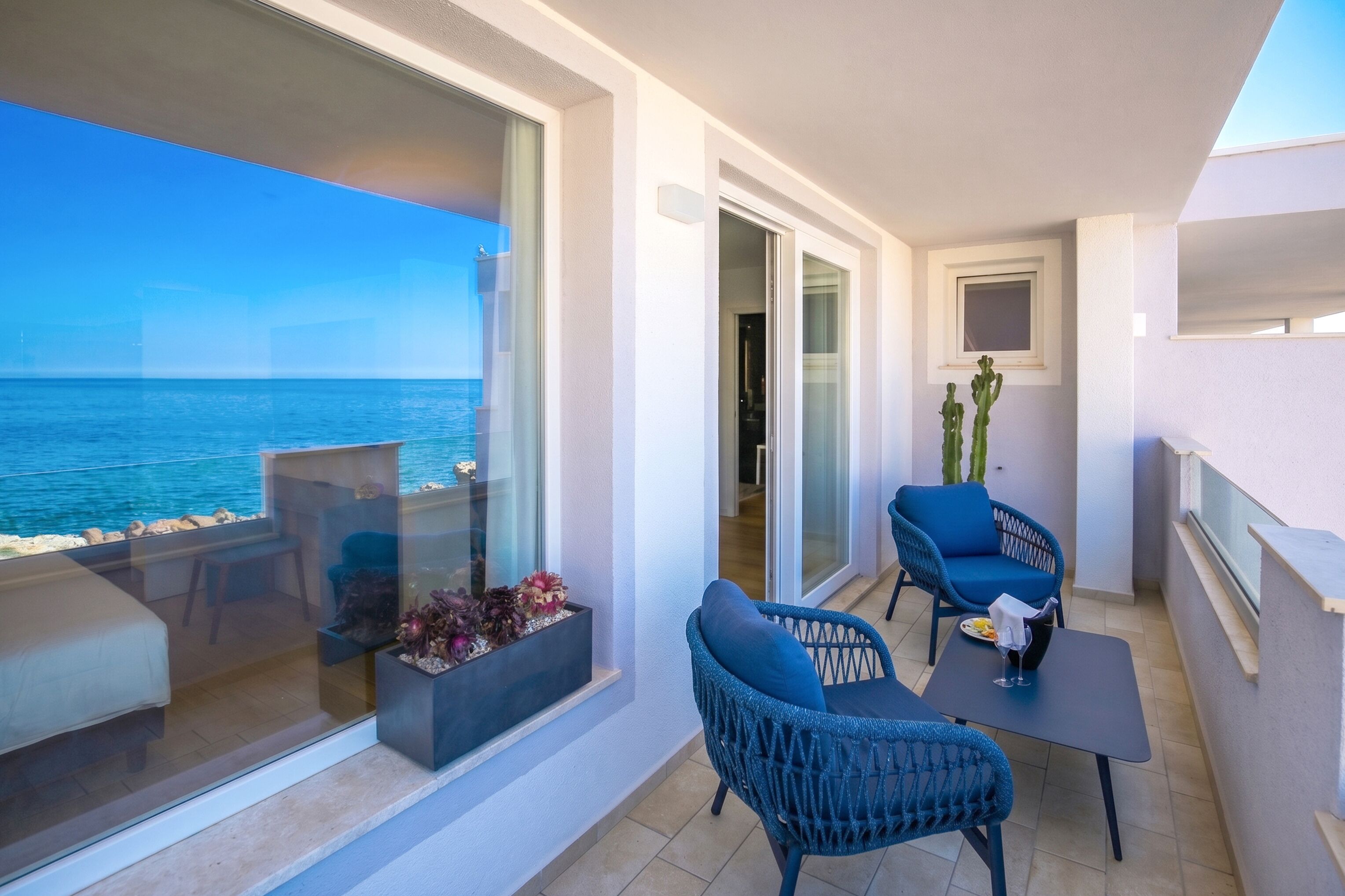Un balcón con vista al mar, un sofá, dos sillones, una mesa y una ventana con una planta.