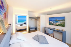 Ein modernes Hotelzimmer mit Bett, Schreibtisch, Stuhl, Fernseher und einem Gemälde einer Küstenlandschaft.