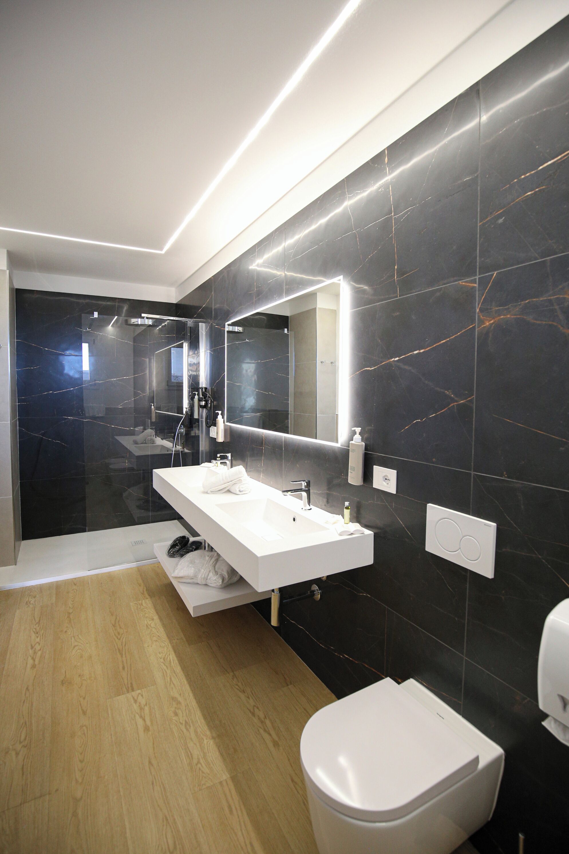 Une salle de bain moderne avec un meuble-lavabo blanc, un grand miroir et des toilettes blanches.