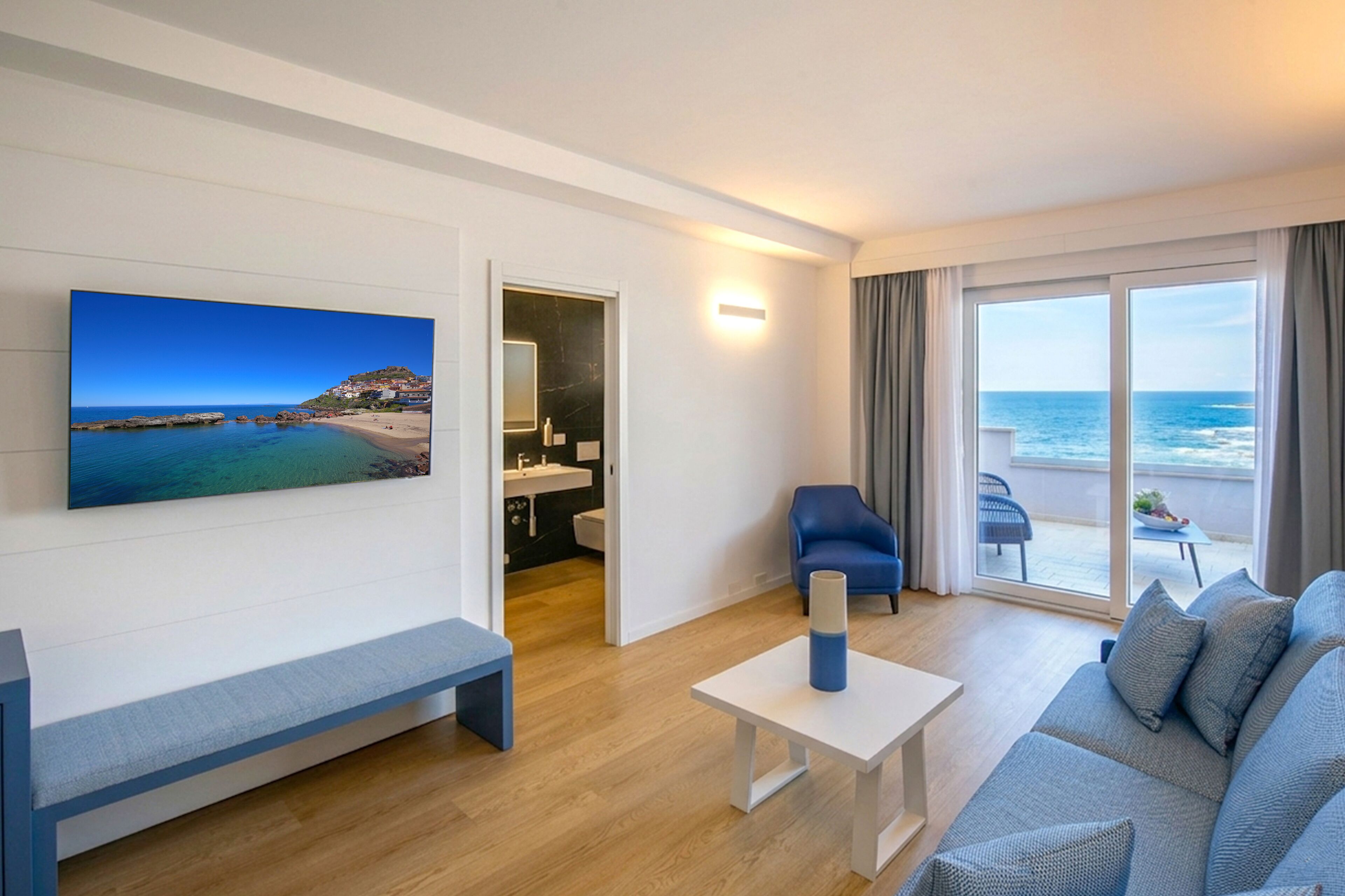 A modern hotel room with a balcony, a large window, a sofa, a coffee table, and a painting of a beach scene.