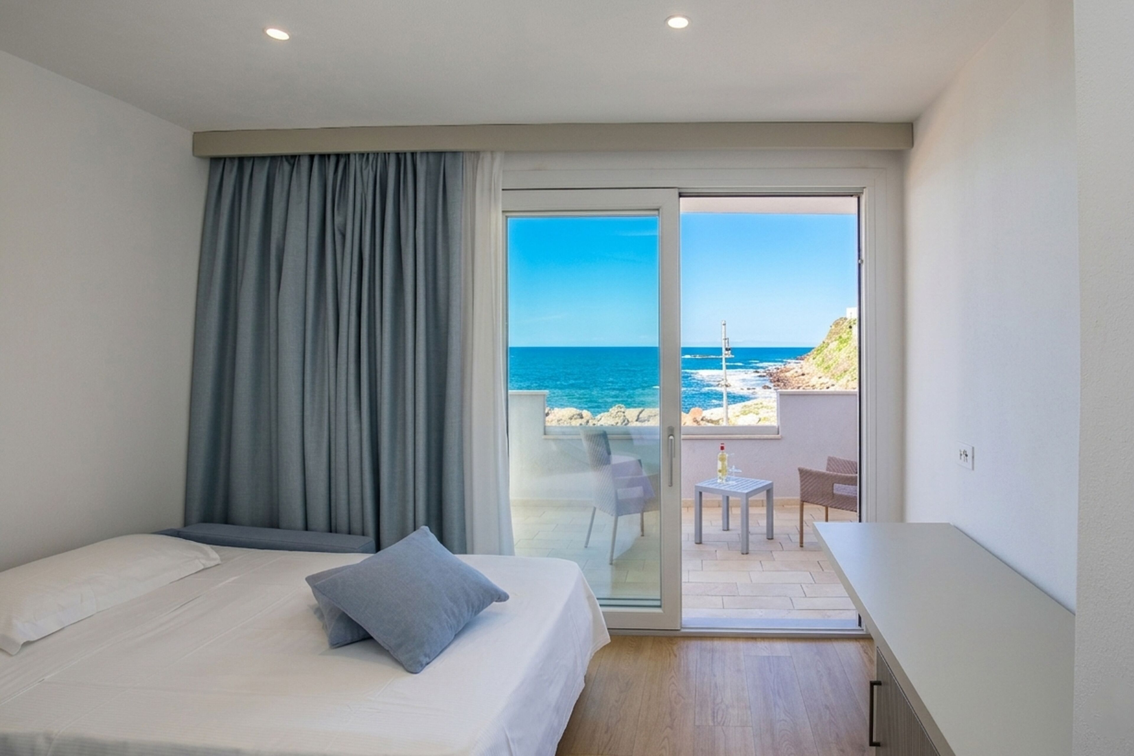 A bedroom with a bed, a view of the sea, and a balcony with a table and chairs.