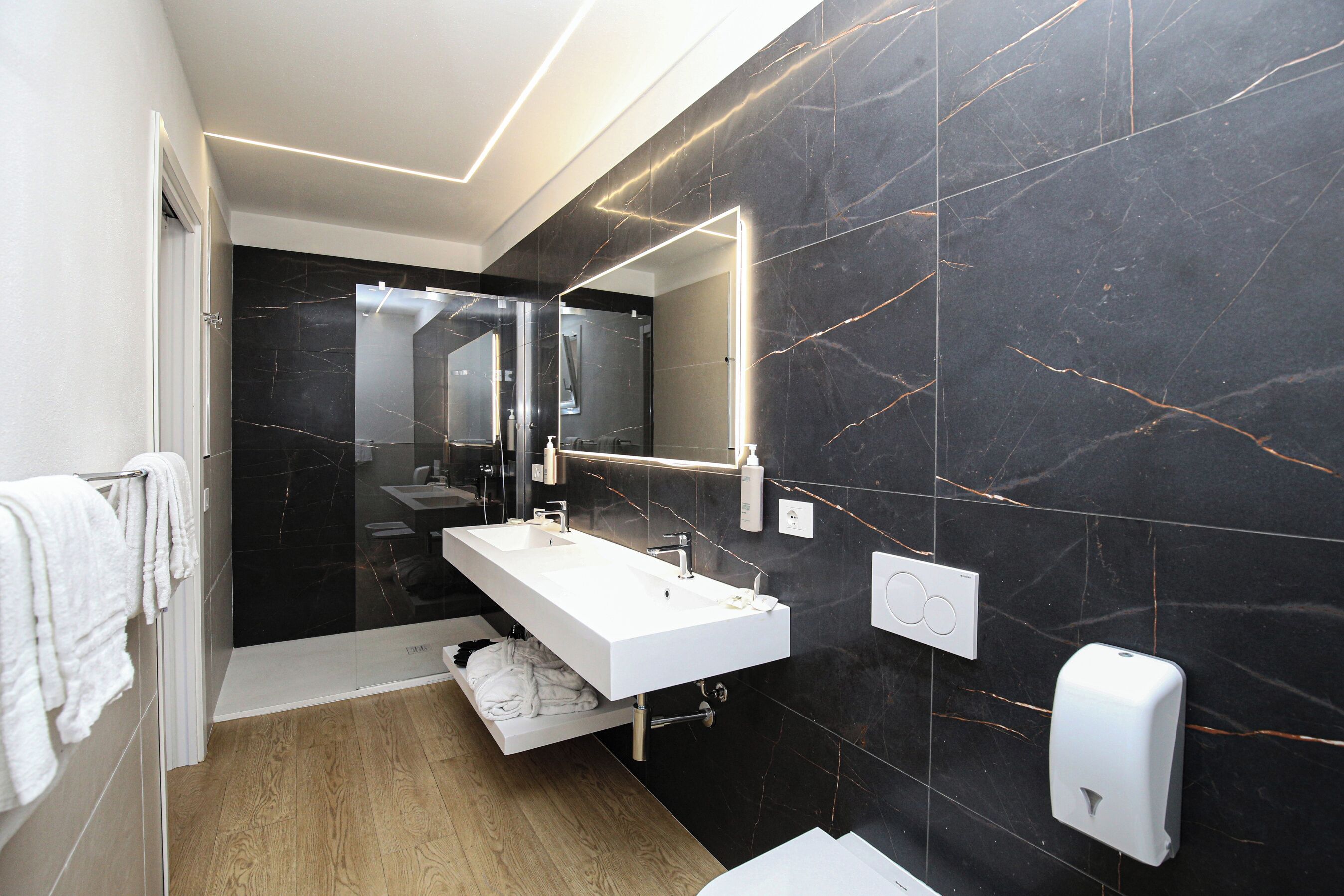 Un bany modern amb un lavabo llarg i blanc, un mirall i un assecagats mans.