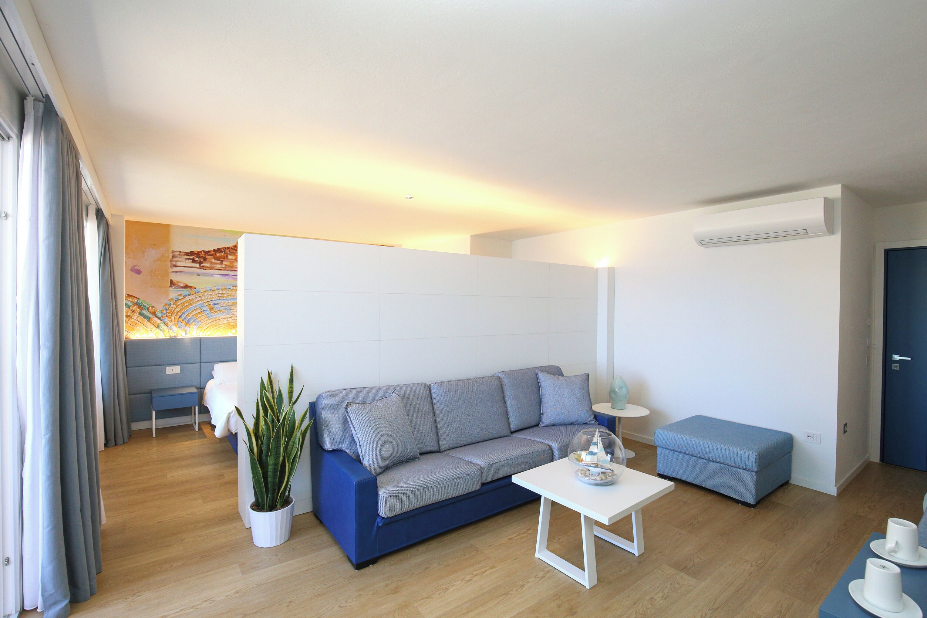 Una sala de estar moderna con un sofá, una mesita, una planta en maceta y un aire acondicionado instalado en la pared.