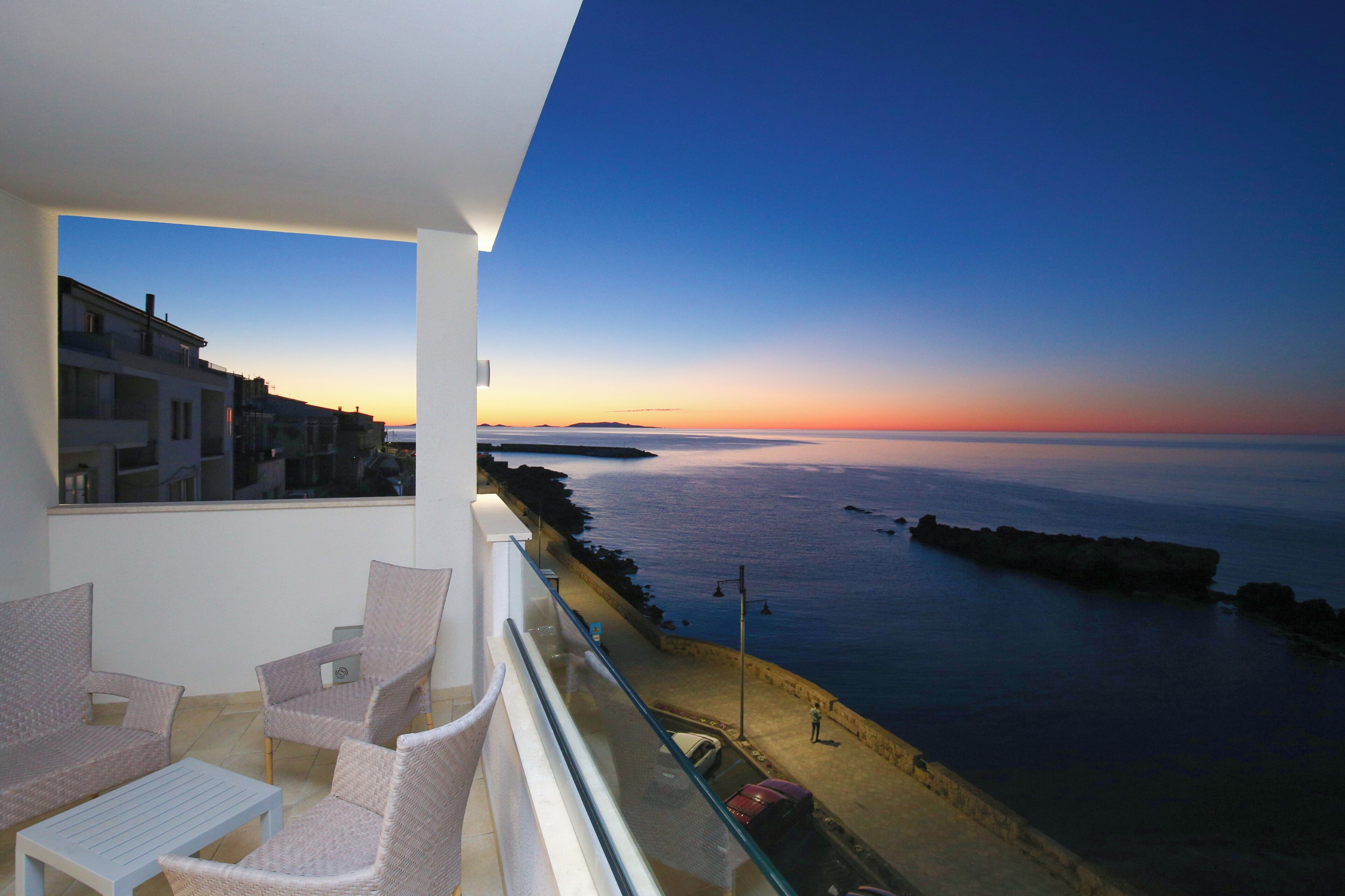 A balcony with wicker furniture, a view of the sea, and a rocky coastline.