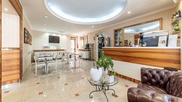 Un vestíbulo de hotel con mostrador de recepción, zona de comedor y área de descanso con sofá de cuero.