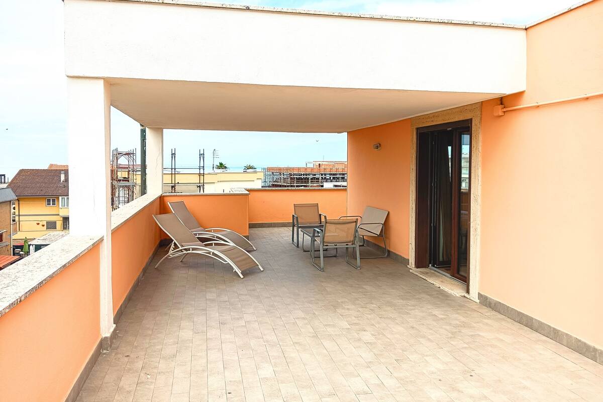 Een balkon met betegelde vloer, twee loungestoelen, een klein tafeltje en een deur.