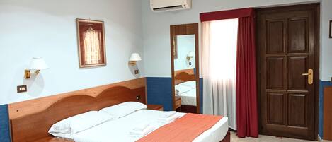 A hotel room with a wooden bed, a nightstand, a mirror, an air conditioning unit, and a door.