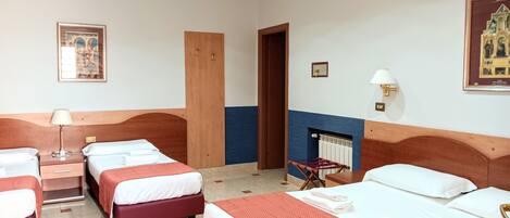 Habitación de hotel con cuatro camas, cabecero de madera, una mesita con lámpara, un cuadro en la pared y una chimenea.