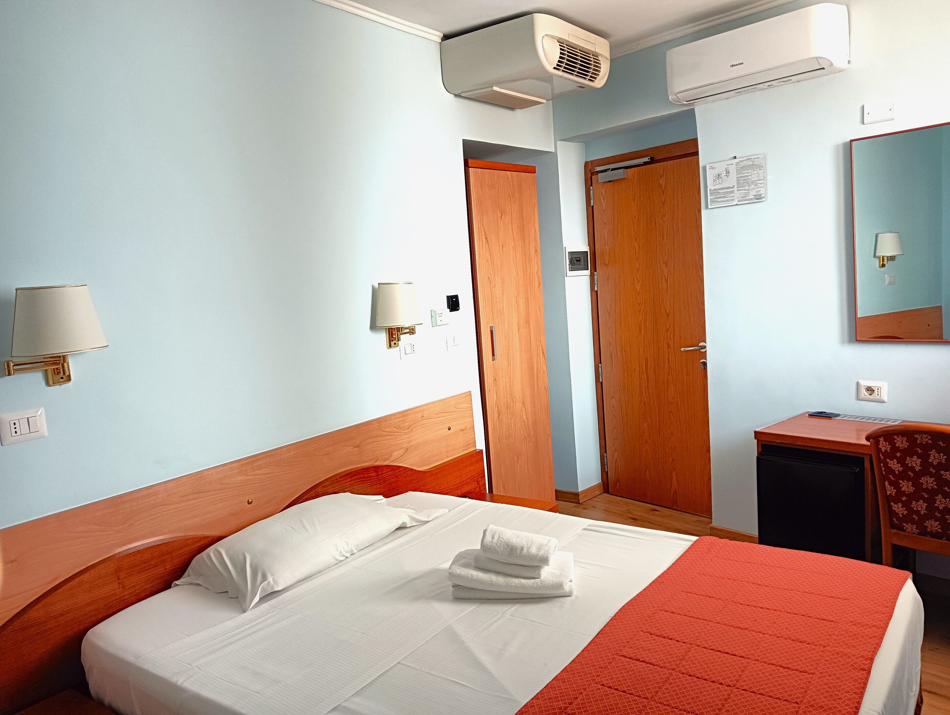 Une chambre d’hôtel équipée d’un lit, d’un bureau, d’une chaise, d’un climatiseur et d’un miroir.