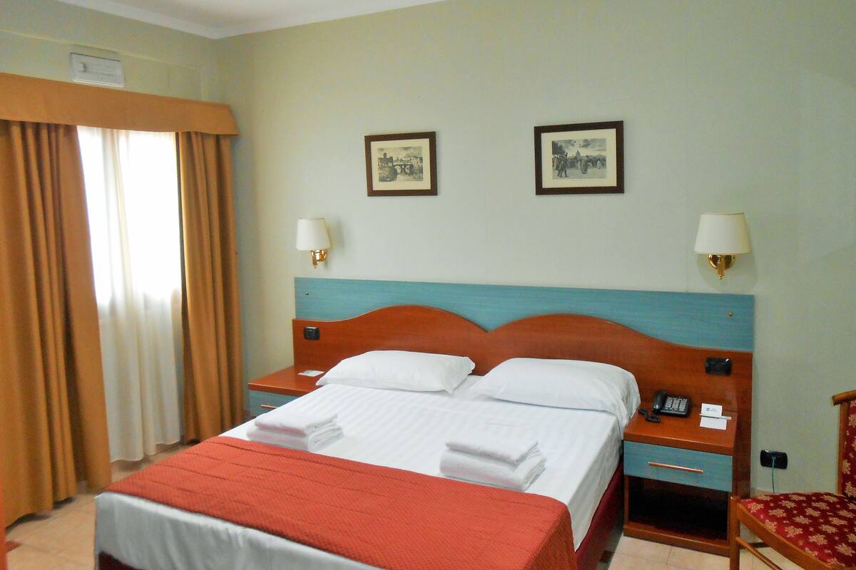 Een hotelkamer met een bed, twee nachtkastjes, een stoel en twee wandlampen.