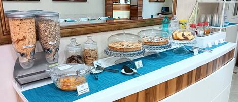 Un mostrador de buffet amb diferents aliments, incloent cereals, galetes i postres, amb un revestiment de rajoles blaves i panells de fusta.