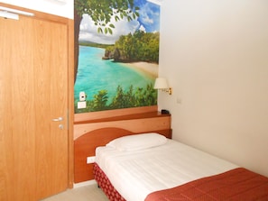 A bedroom with a bed, a wooden door, a wall-mounted lamp, and a mural of a beach scene.