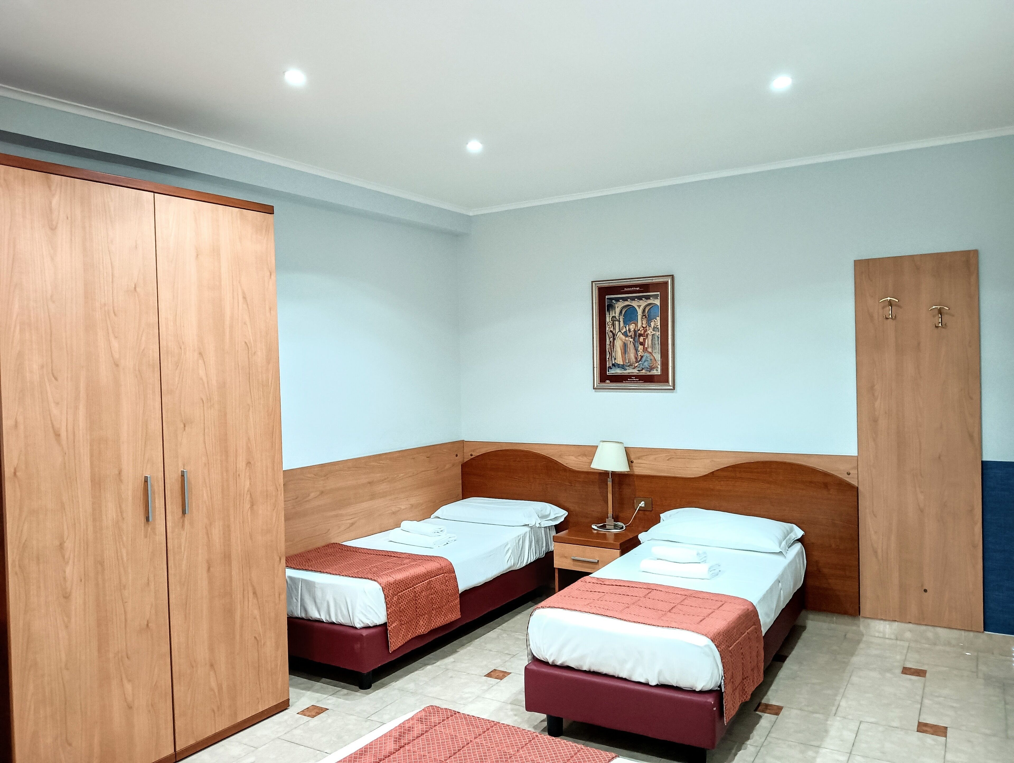 Una habitación con dos camas, un armario de madera, una mesita de noche y una lámpara fijada a la pared.