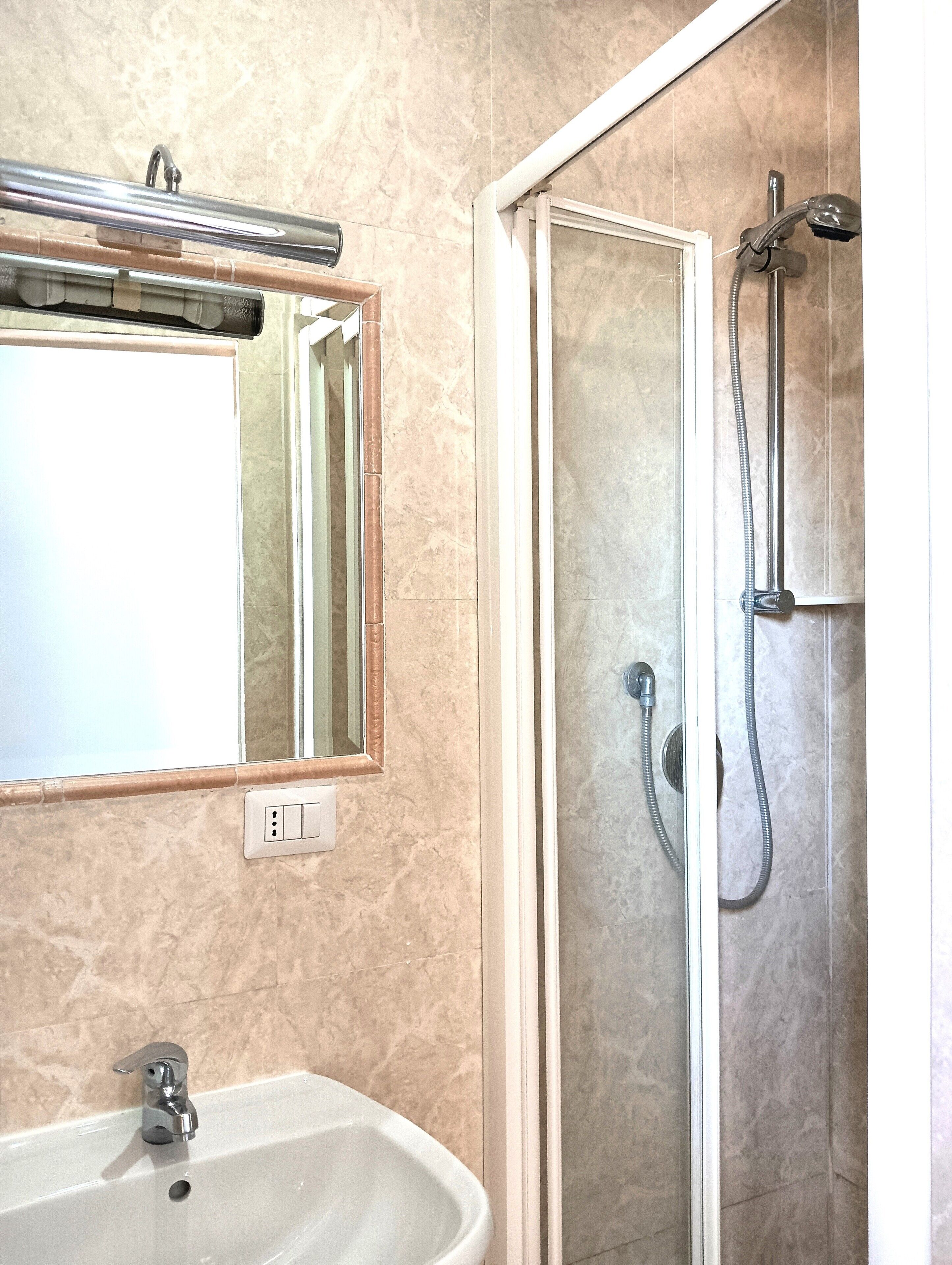 A bathroom with a sink, mirror, shower, and tiled walls.