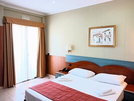 Quarto de hotel com cama, mesa de cabeceira, abajur e um quadro na parede.