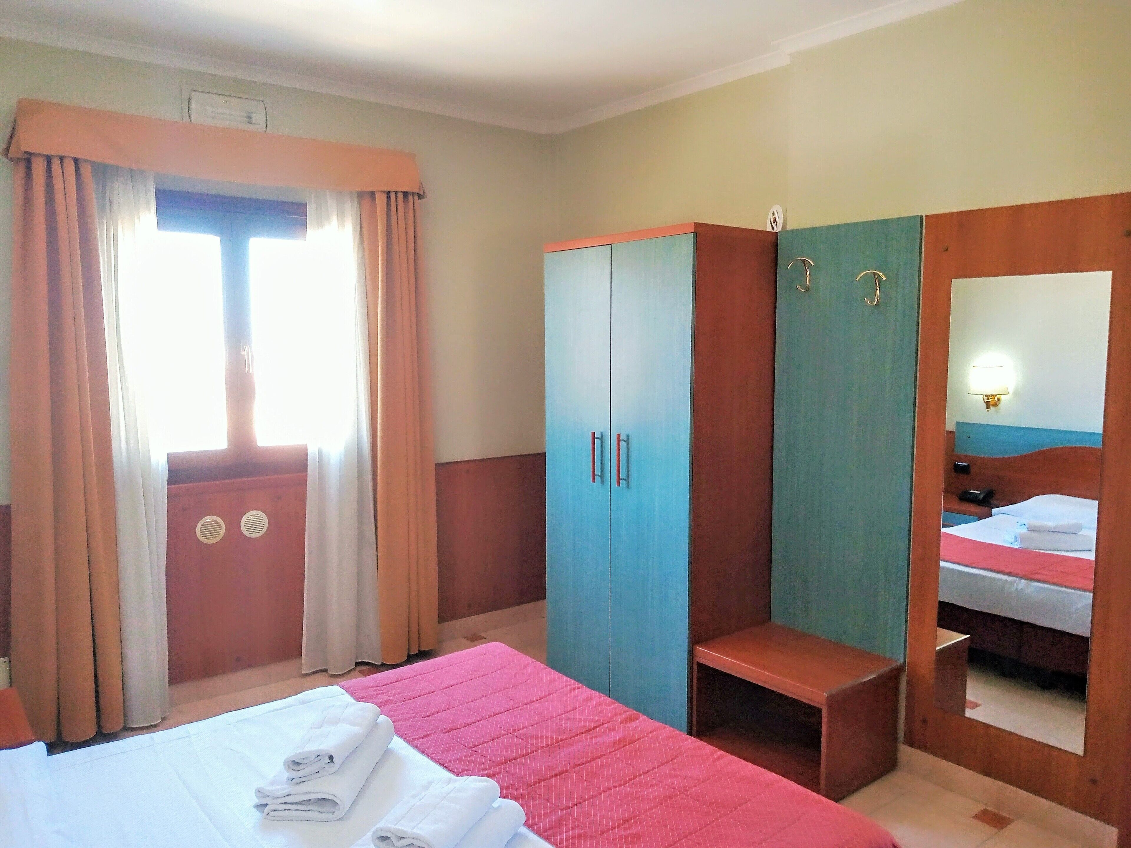 Une chambre d’hôtel avec un lit, une armoire, un banc et un miroir.