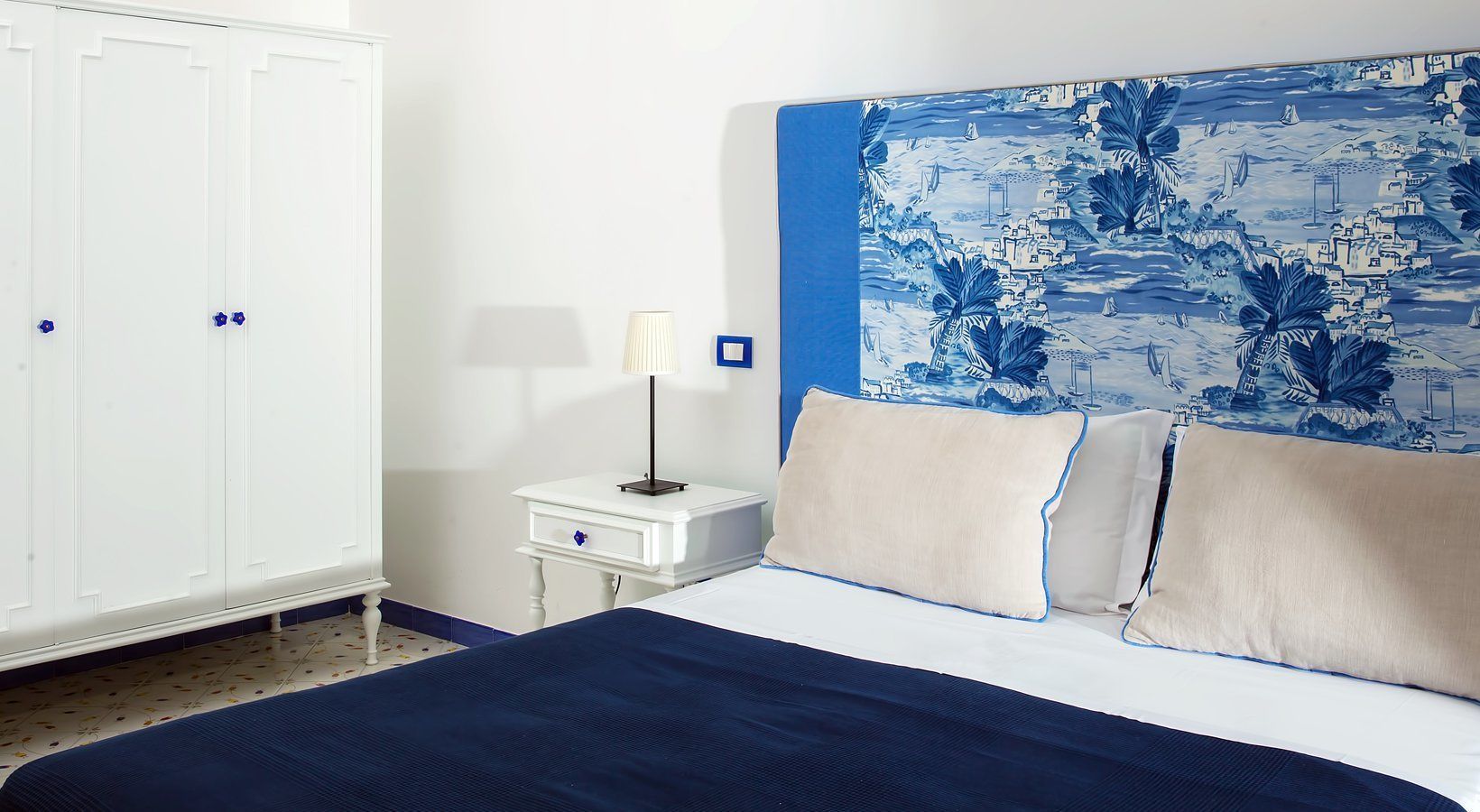 A bedroom with a large bed, white wardrobe, and a nightstand with a lamp.