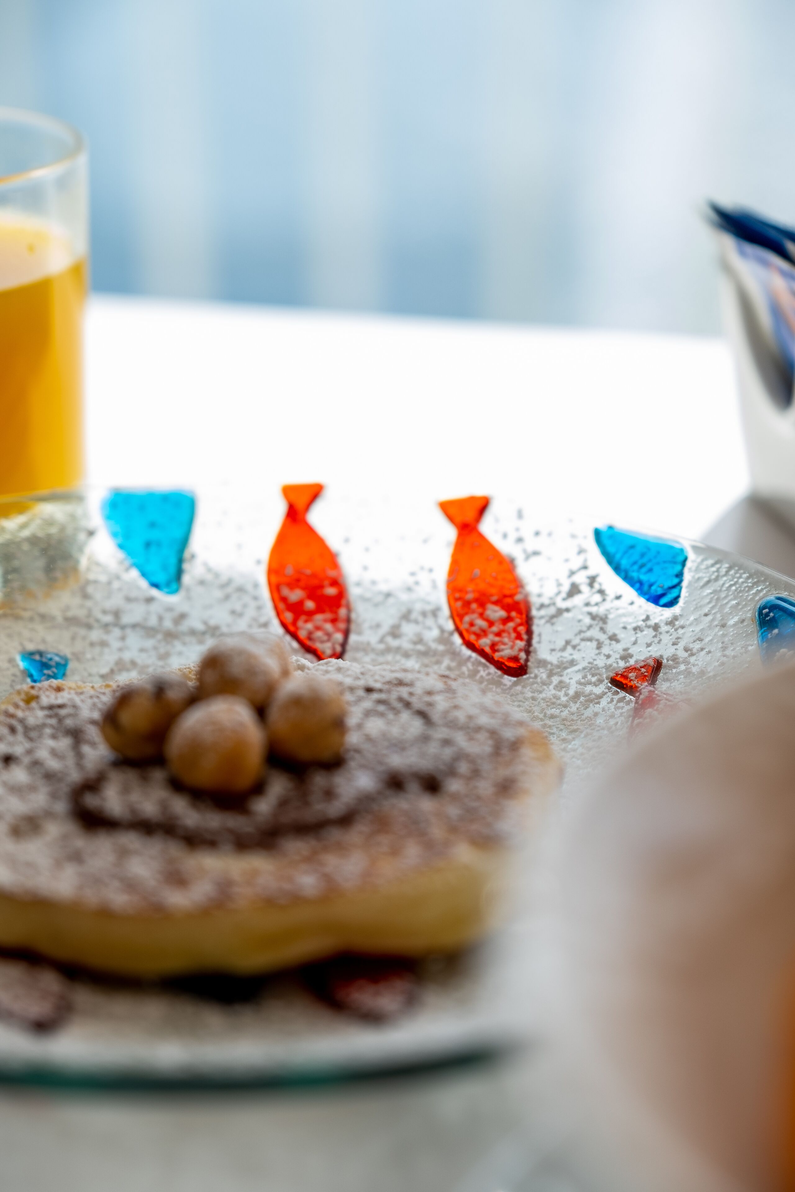 A dessert plate with colorful fish-shaped candies and a glass of orange juice on a table.