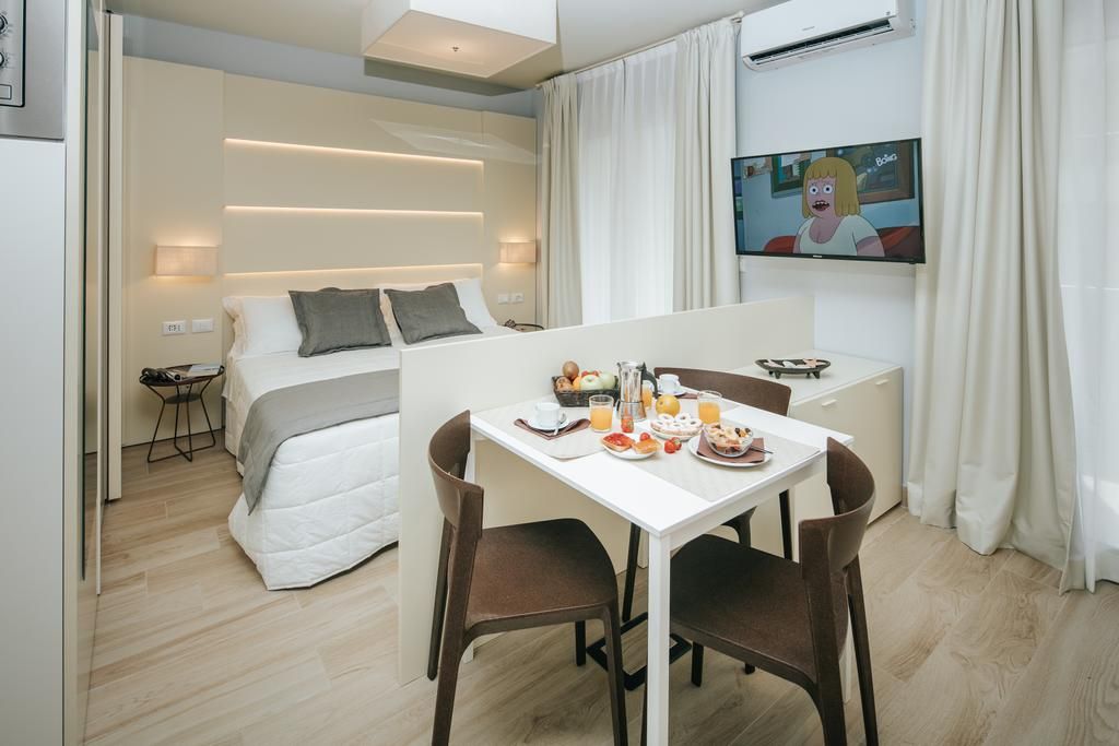 A hotel room with a bed, a dining table with breakfast, a TV, and a window with curtains.