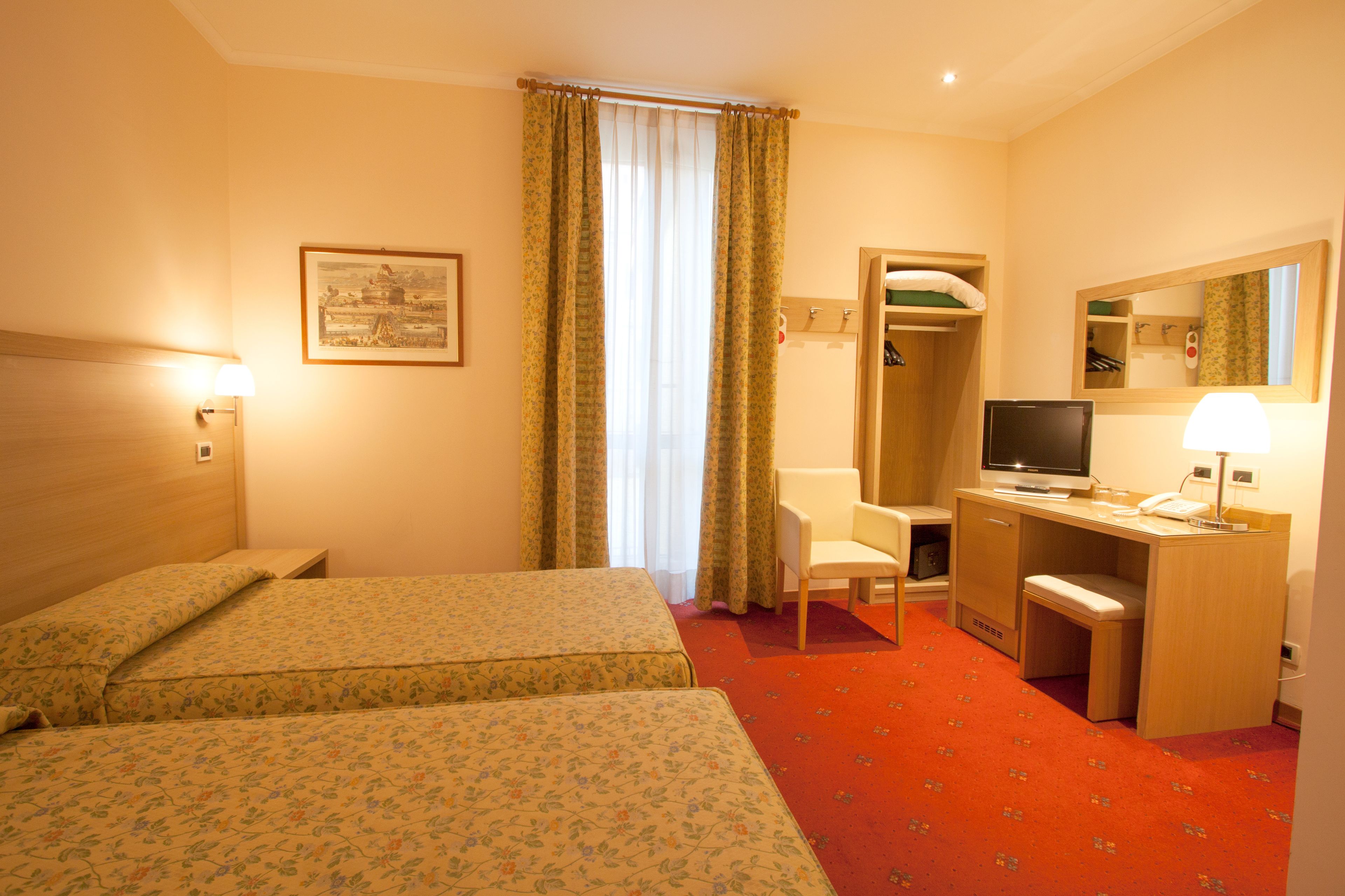 A hotel room with two beds, a desk, a chair, a television, and a mirror.