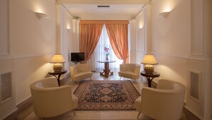 Una habitación de hotel con un tapete grande y decorativo, dos sillones, una mesita redonda y un televisor.