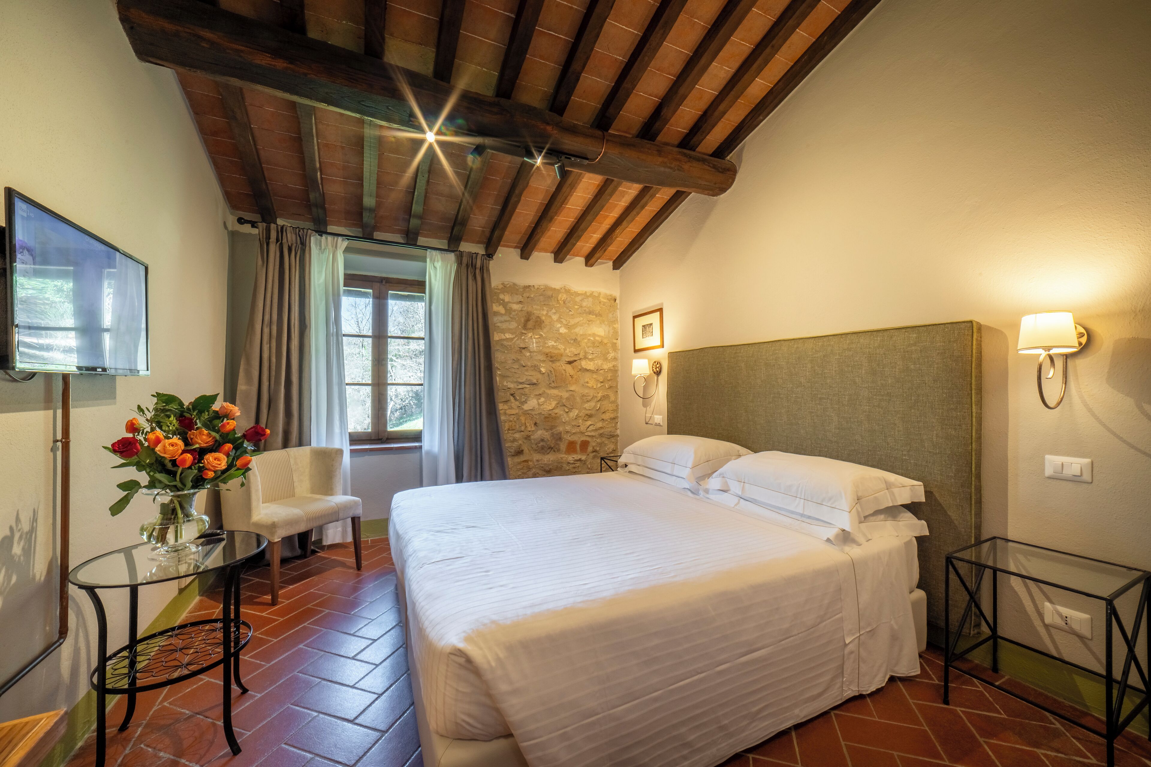 Una camera da letto con un letto grande, una sedia, un tavolino, una TV e un muro in pietra.