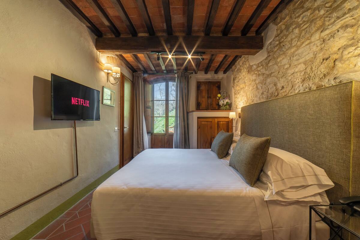 Un dormitorio con una cama, un televisor montado en la pared y una pared de piedra.