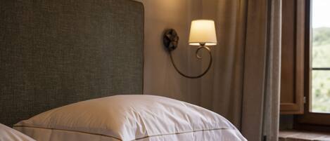 Una cama bien hecha con sábanas blancas y un cabecero, una lámpara de pared y una ventana con cortinas.