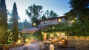 An outdoor dining area with stone walls, tables, and chairs, surrounded by greenery and a stone building in the background. - Ultimo Mulino Wellness Country Hotel (Gaiole in Chianti)