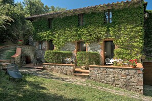 A stone building with ivy-covered walls, a patio with outdoor seating, and a stone staircase leading to the entrance.