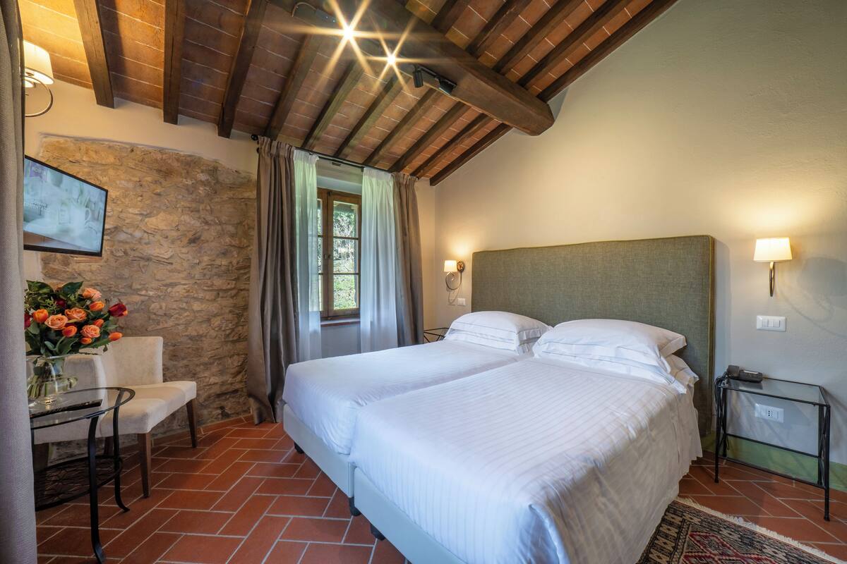 Un dormitorio con una cama grande, un escritorio con silla, una pared de piedra y una ventana con cortinas.