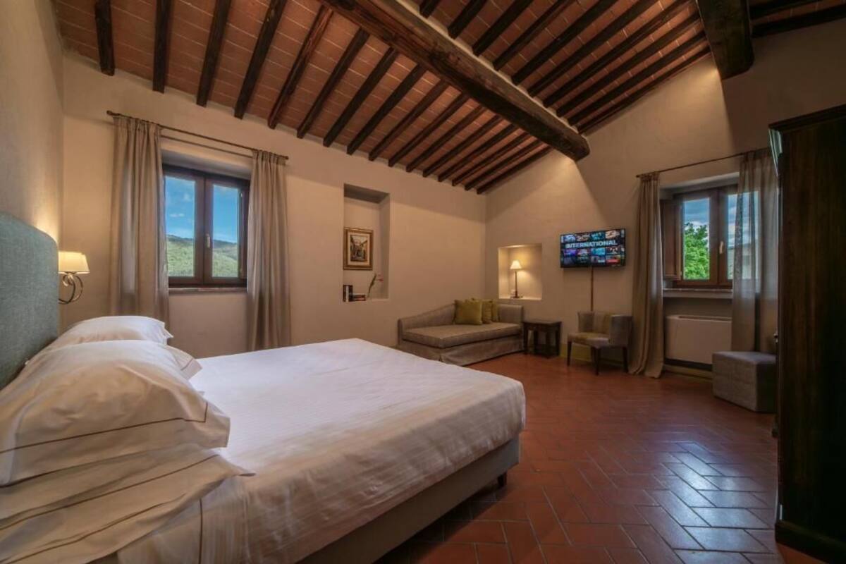 Un dormitorio con cama, sofá, televisor y ventana con cortinas.