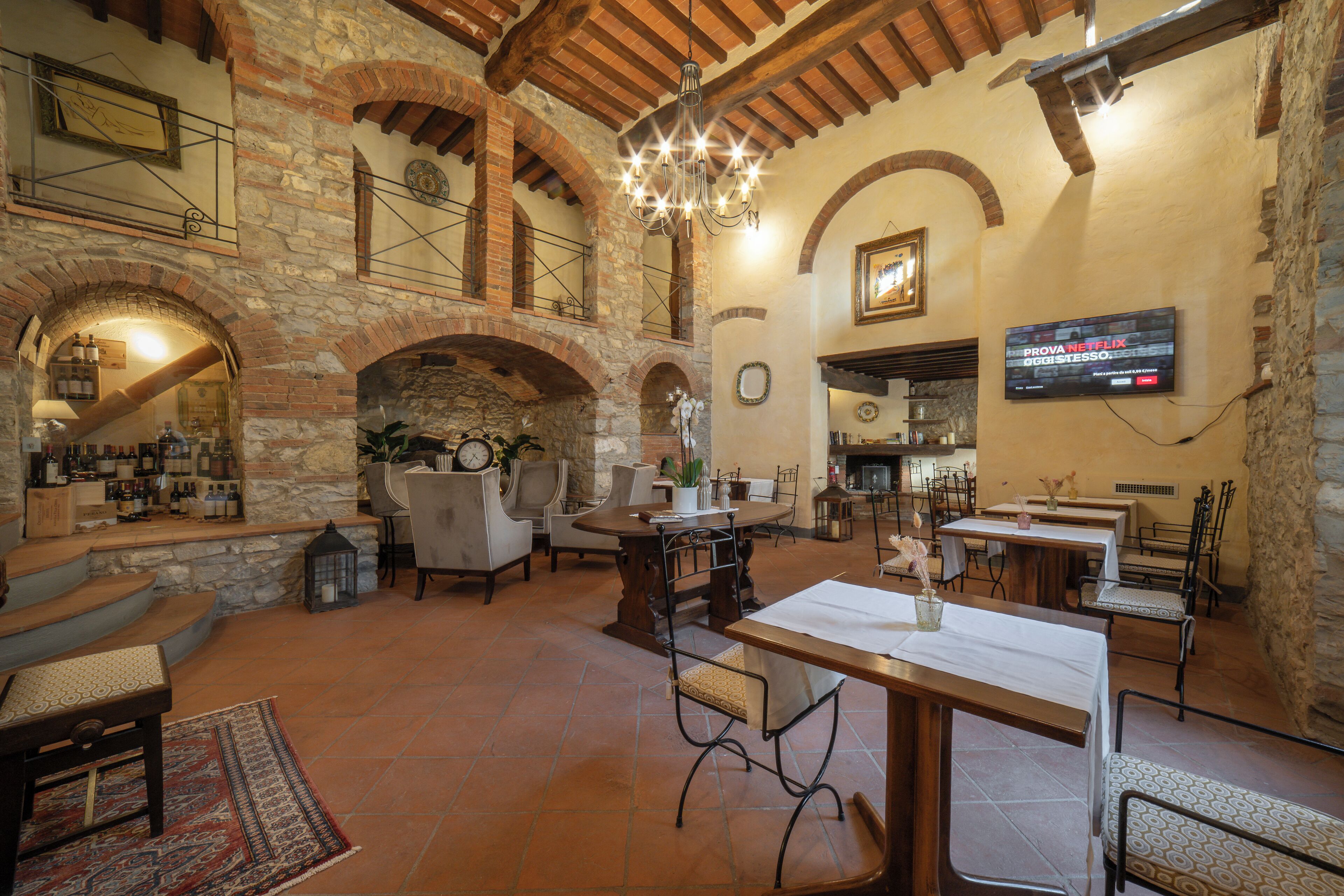 A spacious dining area with high ceilings, stone walls, and a chandelier. Tables and chairs are arranged for dining.