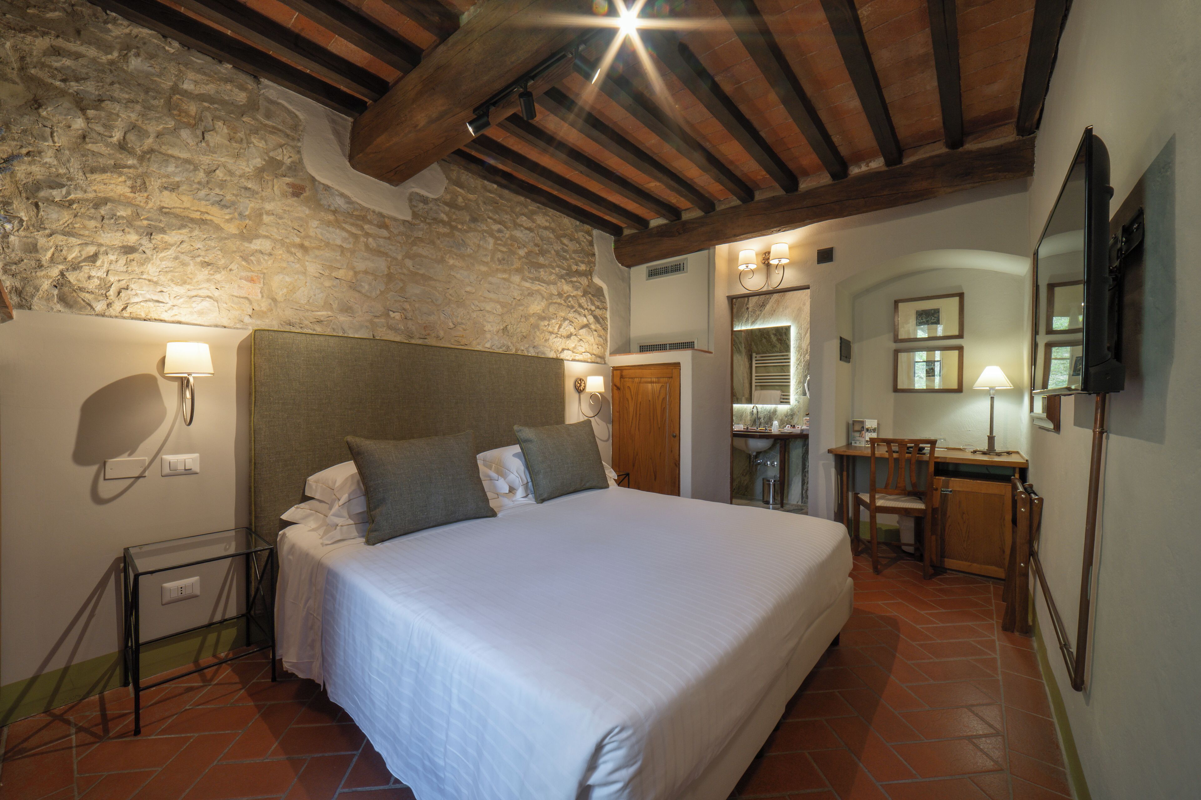 A bedroom with a large bed, a wooden headboard, a stone wall, and a desk with a chair.