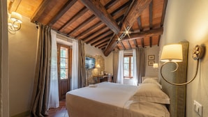 A bedroom with a large bed, wooden beams, stone wall, and a stone fireplace. - Ultimo Mulino Wellness Country Hotel (Gaiole in Chianti)