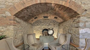 A cozy seating area with two chairs and a table, a stone wall, and a clock on a pedestal. - Ultimo Mulino Wellness Country Hotel (Gaiole in Chianti)