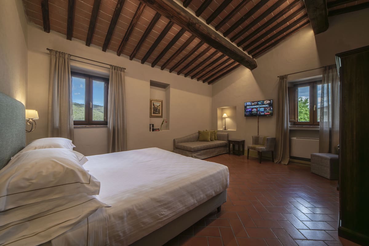 Un dormitorio con una cama grande, un sofá, un televisor y una ventana con cortinas.